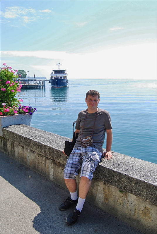 18 - A person wearing a casual gray t-shirt and plaid cargo shorts while sitting on a stone wall by the water